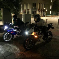 two people on motorcycles parked in front of a building at night with one person wearing a helmet