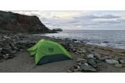 a green tent sitting on top of a sandy beach next to the ocean and rocky shore