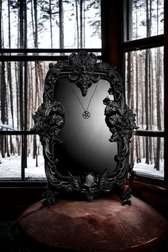 a mirror sitting on top of a wooden table in front of a window covered in snow