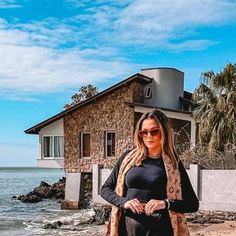 a woman standing on the beach in front of a house