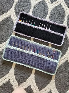 three crocheted pins sitting on top of a gray and white rug next to a person's hand