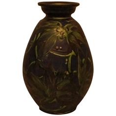 a black vase with green leaves and a flower on the inside is shown against a white background