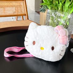 a hello kitty purse sitting on top of a table next to a vase with flowers