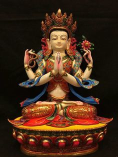 a buddha statue sitting on top of a red and yellow box with two hands in the air