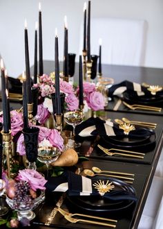 a long table with black and gold place settings, pink flowers and candles on it