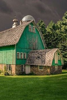 a large green barn sitting in the middle of a lush green field with dark clouds