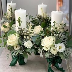 white flowers and greenery are arranged in vases on a table with candles behind them