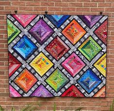 a colorful quilt hanging on the side of a brick wall next to a potted plant