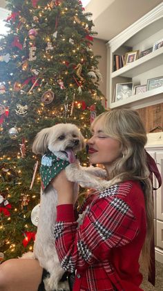 a woman holding a dog in front of a christmas tree