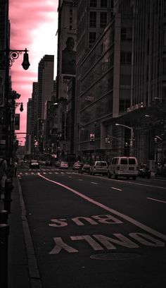 an empty city street with cars parked on the side and tall buildings in the background