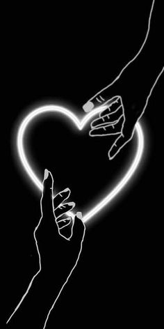 two hands holding a heart shaped object in black and white with neon lights on it