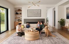 three people sitting on a couch in a living room with a dog looking at them