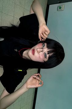 a woman with long black hair standing next to a wall