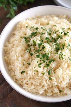 a white bowl filled with rice and garnished with parsley on the side