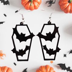 the earrings are decorated with bats and pumpkins on white surface next to halloween decorations