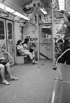 black and white photograph of people sitting on subway cars with graffiti all over the walls