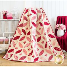 a red and white quilt sitting on top of a wooden floor next to a table