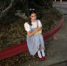 a woman sitting on the side of a road next to a red curb at night