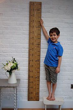 a young boy standing next to a tall wooden ruler on top of a white table