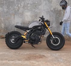 a motorcycle parked next to a wall with a person in the background walking past it