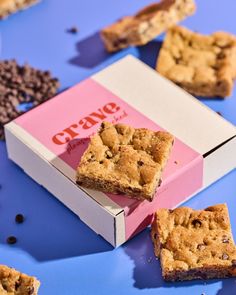 three pieces of chocolate chip cookie sitting in a pink box on a blue surface with other cookies scattered around it