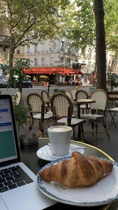 an open laptop computer sitting on top of a table next to a croissant