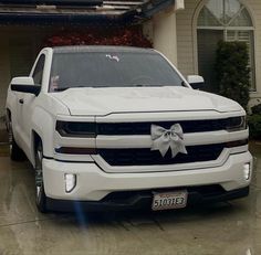 a white truck parked in front of a house with a bow on it's hood