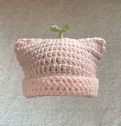 a pink crocheted pillow with a small green plant on the top of it