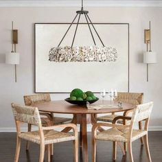 a dining room table with chairs and a bowl of fruit on it in front of a painting