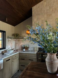 a vase filled with blue flowers sitting on top of a wooden table in a kitchen