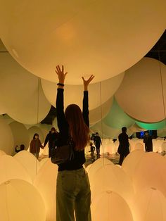 a woman standing in front of giant white balls with her hands up to the sky