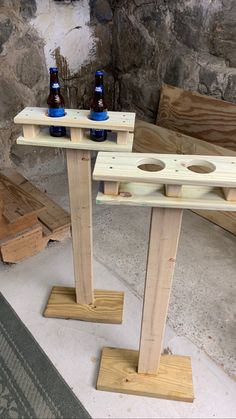 two beer bottles sitting on top of wooden posts in front of a stone wall and bench