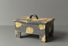 a small wooden box sitting on top of a gray table next to a black wall