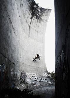 a man riding a bike up the side of a cement wall with graffiti on it