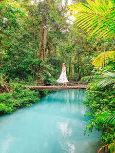 a woman standing on a bridge in the middle of a river surrounded by lush green trees