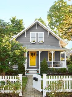 a gray house with white picket fence and yellow door in the front yard is featured in this magazine