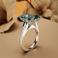 a ring with a blue topazte surrounded by white diamonds sits on a table next to flowers