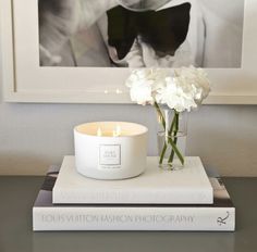 white flowers are in a vase on top of two books and a candle is next to it