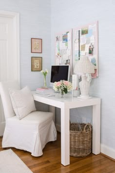 a white desk topped with a computer monitor next to a chair and vase filled with flowers