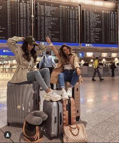 two women sitting on suitcases at an airport posing with their arms in the air