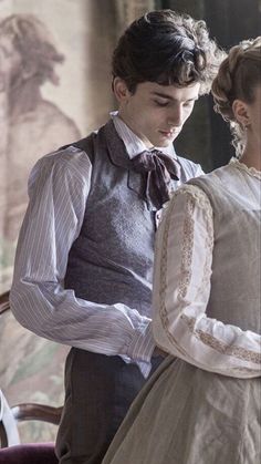 the young man and woman are dressed up in period clothing, looking down at something