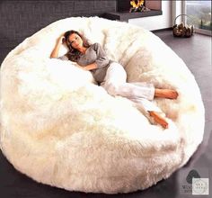 a woman laying on top of a large white bean bag chair in a living room