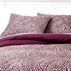 a bed with purple and white comforters on top of it next to a night stand