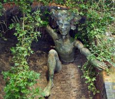 a statue is sitting in the middle of some bushes and ivys, with one hand on his head