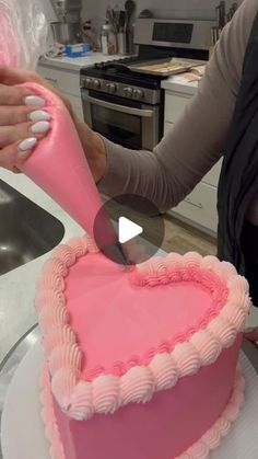 a woman cutting a heart shaped cake with a pink knife on top of the cake