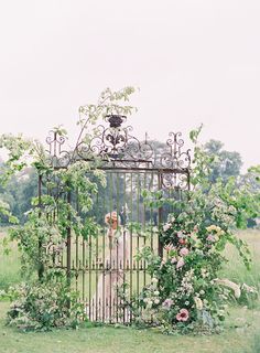 a woman standing in front of an iron gate with vines and flowers on the sides