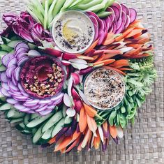 an arrangement of vegetables and dips on a wicker surface