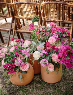 two vases filled with pink and white flowers on top of grass next to wooden chairs