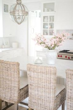 a white kitchen with wicker chairs and a chandelier hanging from the ceiling