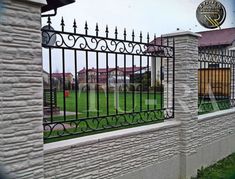 an iron fence is next to a white brick building with a soccer field in the background